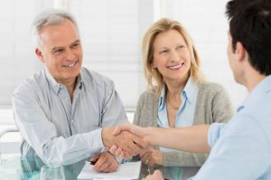 A happy couple shakes a man's hand over paperwork